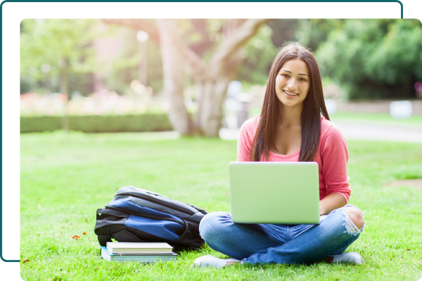 student sitting in grass working on laptop
